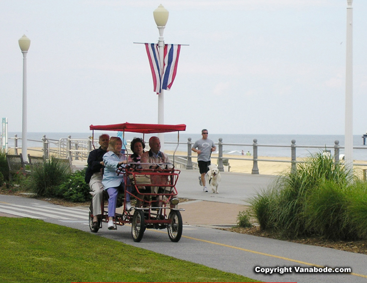 A picture of friends riding a surrey bicycle and runner on boardwalk in Virginia Beach